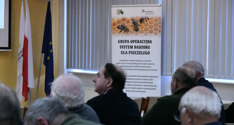 Na zdjęciu uczestnicy wydarzenia, w tle plakat informacyjny Grupy operacyjnej System nadzoru ula pszczelego. 